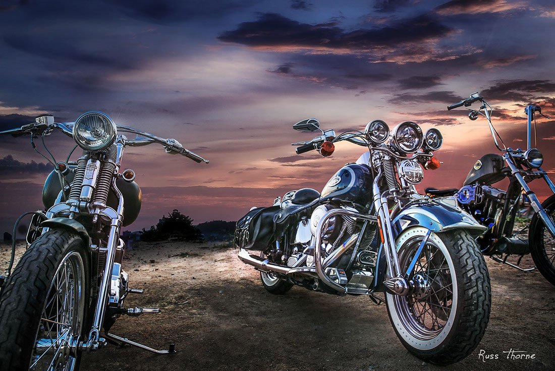 Three custom Harley-Davidson motorcycles displayed against a stunning sunset, showcasing their unique designs and craftsmanship.